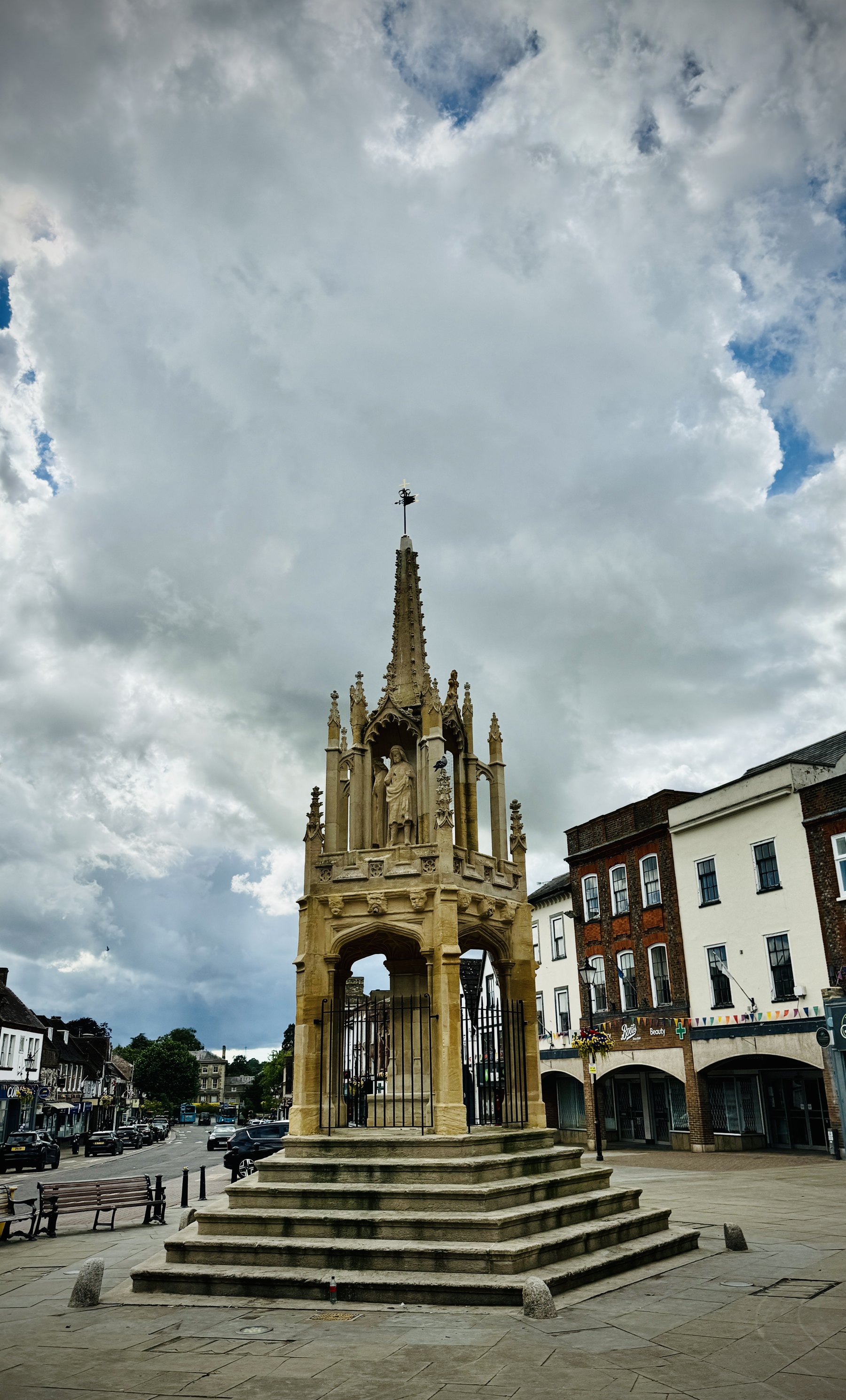 The Market Cross in Leighton Buzzard, with shops around the square beneath a cloudy sky